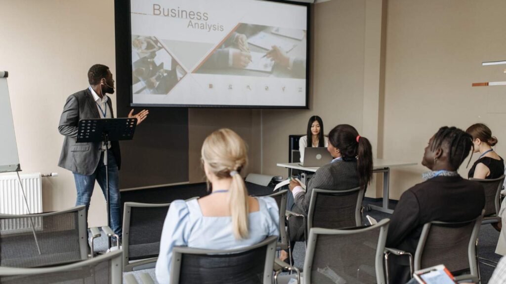 Employees sitting in a conference room attending a virtual HR seminar with a presenter displayed on the screen.